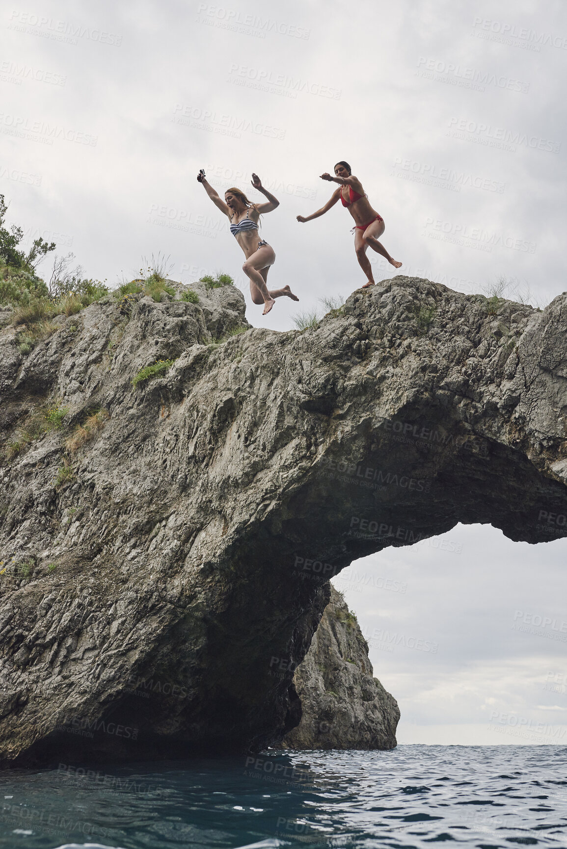 Buy stock photo Cliff, friends and woman jumping in ocean together for holiday, travel or vacation activity. Courage, leap and rocks with people plunge into sea for action, adrenaline or bonding on summer morning