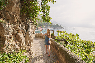 Buy stock photo Woman, travel and explore with flowers by ocean, adventure and back view with coastal city experience. Walk, tourism and female person in nature, flora and seaside walkway space with journey in Italy