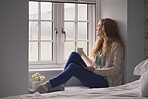 Beautiful red-haired woman relaxing at home using smart phone drinking coffee in window looking out