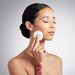 A beautiful mixed race woman using a cotton pad to remove makeup during a selfcare grooming routine. Hispanic woman applying toner to her face against grey copyspace background in a studio