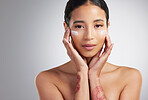 Studio Portrait of a beautiful smiling mixed race woman applying cream to her face. Hispanic model with glowing skin using sunscreen against a grey copyspace background