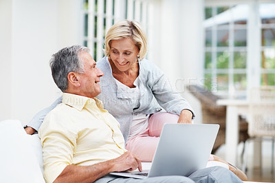 Buy stock photo A pretty senior woman looking at her husband while they use a laptop in the lounge
