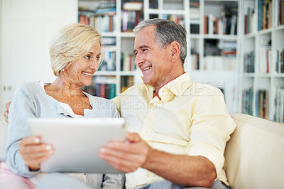 Buy stock photo A senior couple looking at each other while holding a tablet in their home study