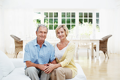 Buy stock photo A senior couple sitting on their couch while smiling at the camera
