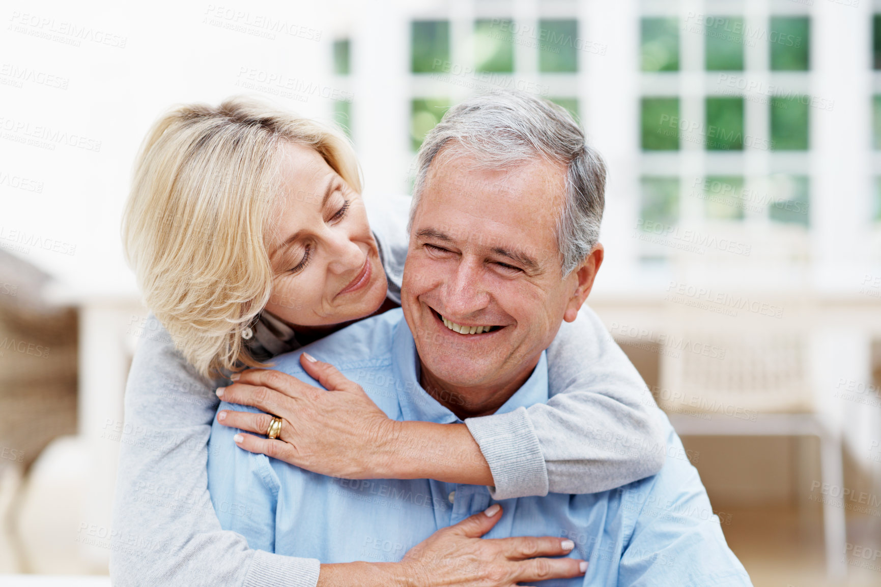 Buy stock photo Old couple, relax and smile at house with hug, love and support for bonding together in lounge. Happy, senior people and embrace in home with security, partner affection and retirement for commitment