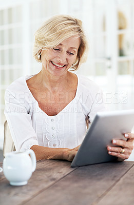 Buy stock photo A smiling senior woman holding a digital tablet while sitting outside with a cup of coffee
