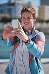Portrait happy young man taking photo using smartphone camera on waterfront sharing summertime on social media with mobile phone