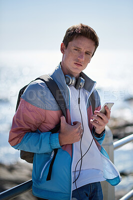 Buy stock photo Man, student and beach with phone on promenade for outdoor network, connection or break. Male person, academic learner or headphones with mobile smartphone, music or bag for audio app on ocean coast