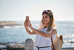 Beautiful travel woman taking photo using smartphone camera on waterfront sharing summer vacation photographing ocean with mobile phone