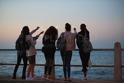 Buy stock photo Sunset, people and sparkler by beach with new year celebration, bonding together and fun holiday. Back, evening and friends outdoor on promenade with ocean, fireworks or travel adventure for vacation