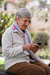 Happy senior woman using smartphone texting browsing messages on mobile phone in beautiful garden