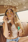 Fun playful hippie girl blowing bubbles in vintage camper van on summer vacation