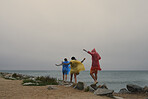 Three friends having fun balancing rocks wearing ponchos in the rain at the seaside