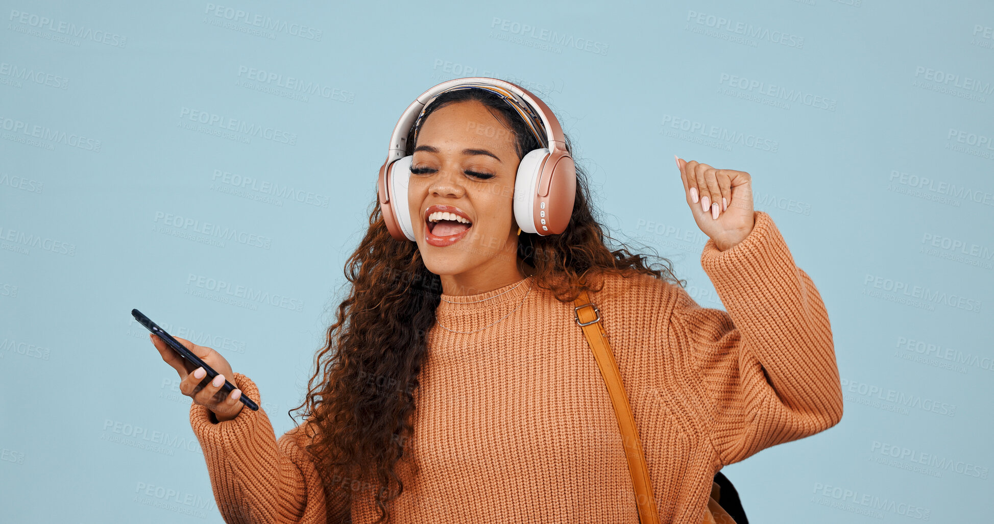 Buy stock photo Cellphone, headphones and woman in studio with dancing, singing and listening to music or playlist. Dance, phone and happy person with audio tech for streaming album on mobile app by blue background