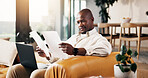 Documents, laptop and remote work with black man on sofa in home living room for finance review. Computer, paperwork and reading with freelance employee in apartment for financial feedback or report
