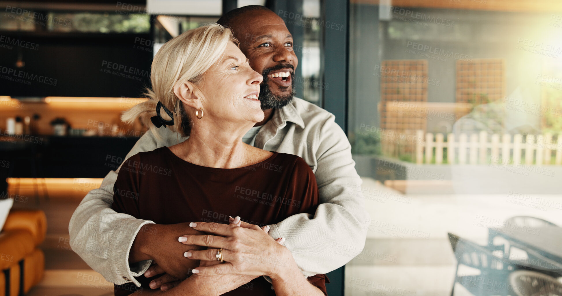 Buy stock photo Interracial couple, hug and window with smile, thinking and love or commitment for relationship. Happy, mature people and security with embrace, romance and space with bonding and partner in home