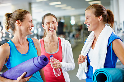 Buy stock photo Shot of three young women with yoga mats talking in a gym