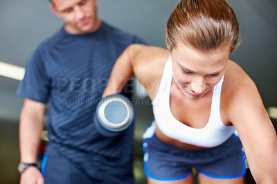 Buy stock photo Shot of a young woman being assisted by a personal trainer while she uses dumbbells