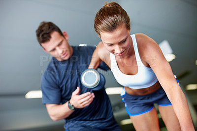 Buy stock photo Shot of a young woman being assisted by a personal trainer while she uses dumbbells