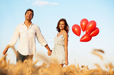 Buy stock photo Balloons, holding hands and love with couple in field for spring date, honeymoon getaway and bonding. Trust, holiday and celebration with man and portrait of woman in countryside for romance and care