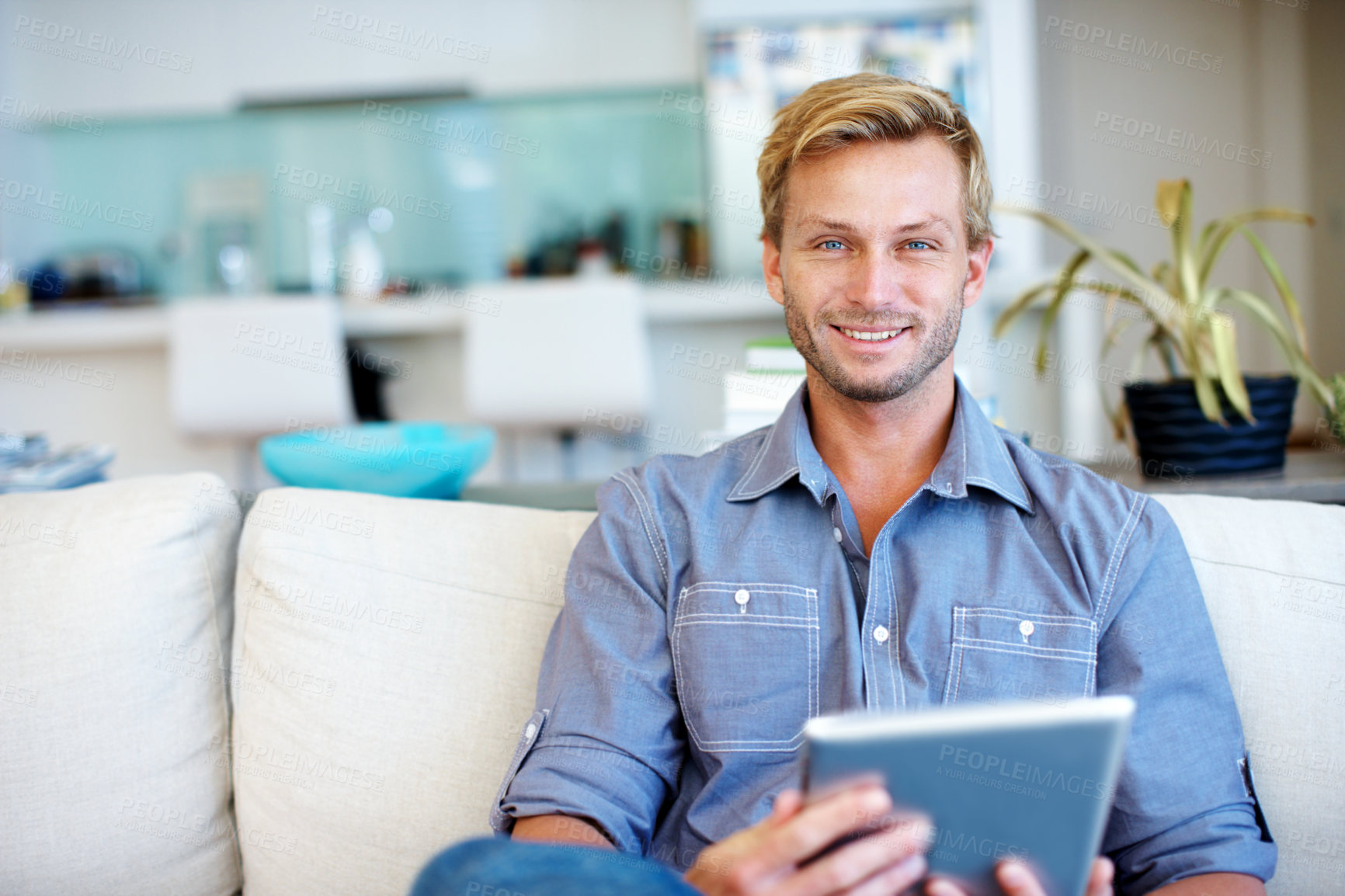 Buy stock photo Handsome young guy using a digital tablet on the sofa at home