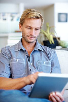 Buy stock photo Handsome young guy using a digital tablet on the sofa at home
