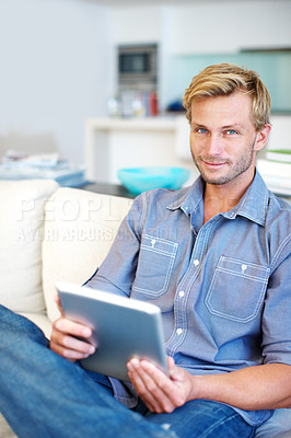 Buy stock photo Handsome young guy using a digital tablet on the sofa at home