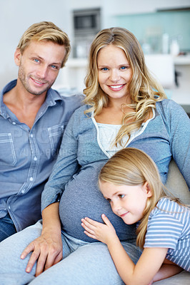 Buy stock photo Cute little girl sitting on the sofa with her father and pregnant mother and listening to her mother's belly