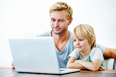 Buy stock photo A little boy sitting at his laptop while his father helps him 