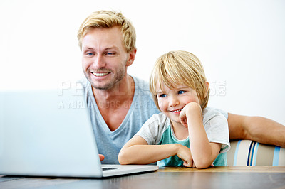 Buy stock photo A little boy sitting at his laptop while his father helps him 