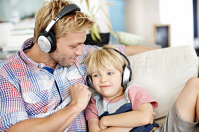 Buy stock photo Cute little boy wearing headphones and listening to music on the sofa with his father