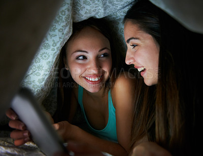 Buy stock photo Two teenage girls sharing a tablet under the blankets at home