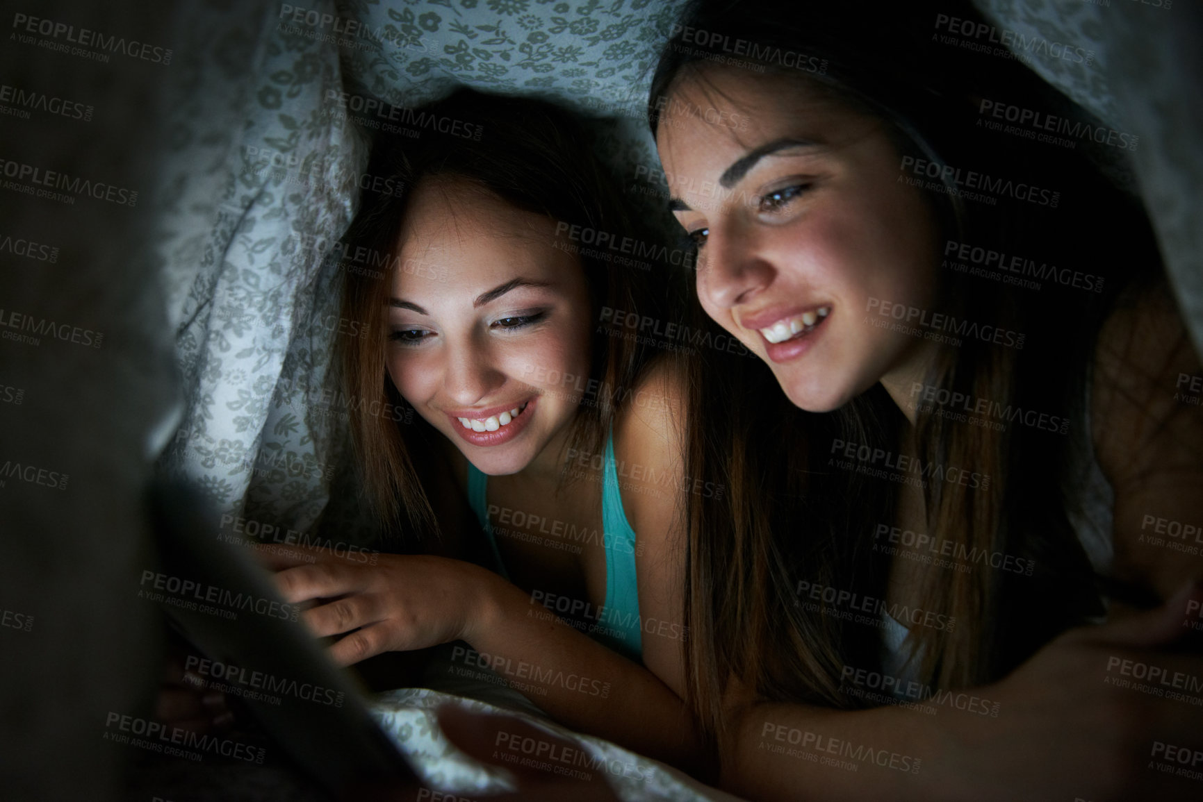Buy stock photo Teenager, blanket and tablet with sisters in home at night for bonding, ebook or social media. Gossip blog, support and online post with girls under covers in family house for relax, late and article