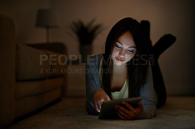 Buy stock photo A teenage girl lying on the floor while reading her e-book