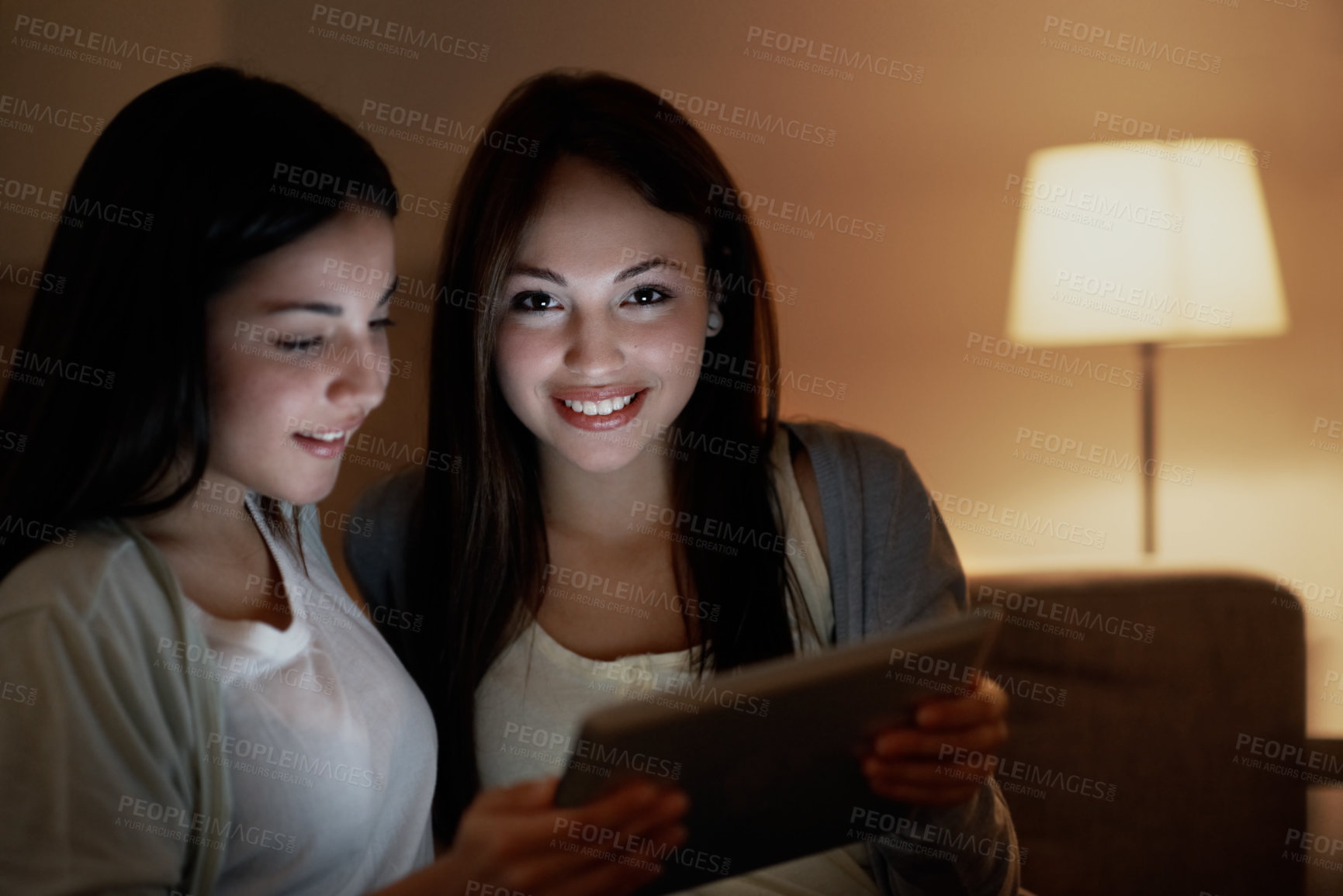 Buy stock photo Teenager, smile and tablet with sisters in home at night for bonding, ebook and social media. Gossip blog, support and online post with portrait of girl in family house for relax, late and article