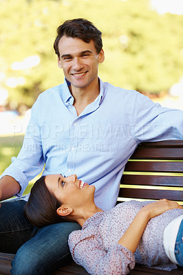Buy stock photo Handsome man smiling at you while sitting with his girlfriend on a park bench 