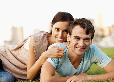 Buy stock photo Happy young couple posing lovingly while lying on some grass in a park