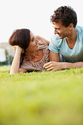 Buy stock photo Low-angle view of a loving couple lying on the grass in a park talking - copyspace