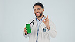 Doctor, phone and portrait with green screen in studio for Telehealth app, mockup or marketing. Man, healthcare worker or smile on space with OK sign, smartphone or advertising on a white background