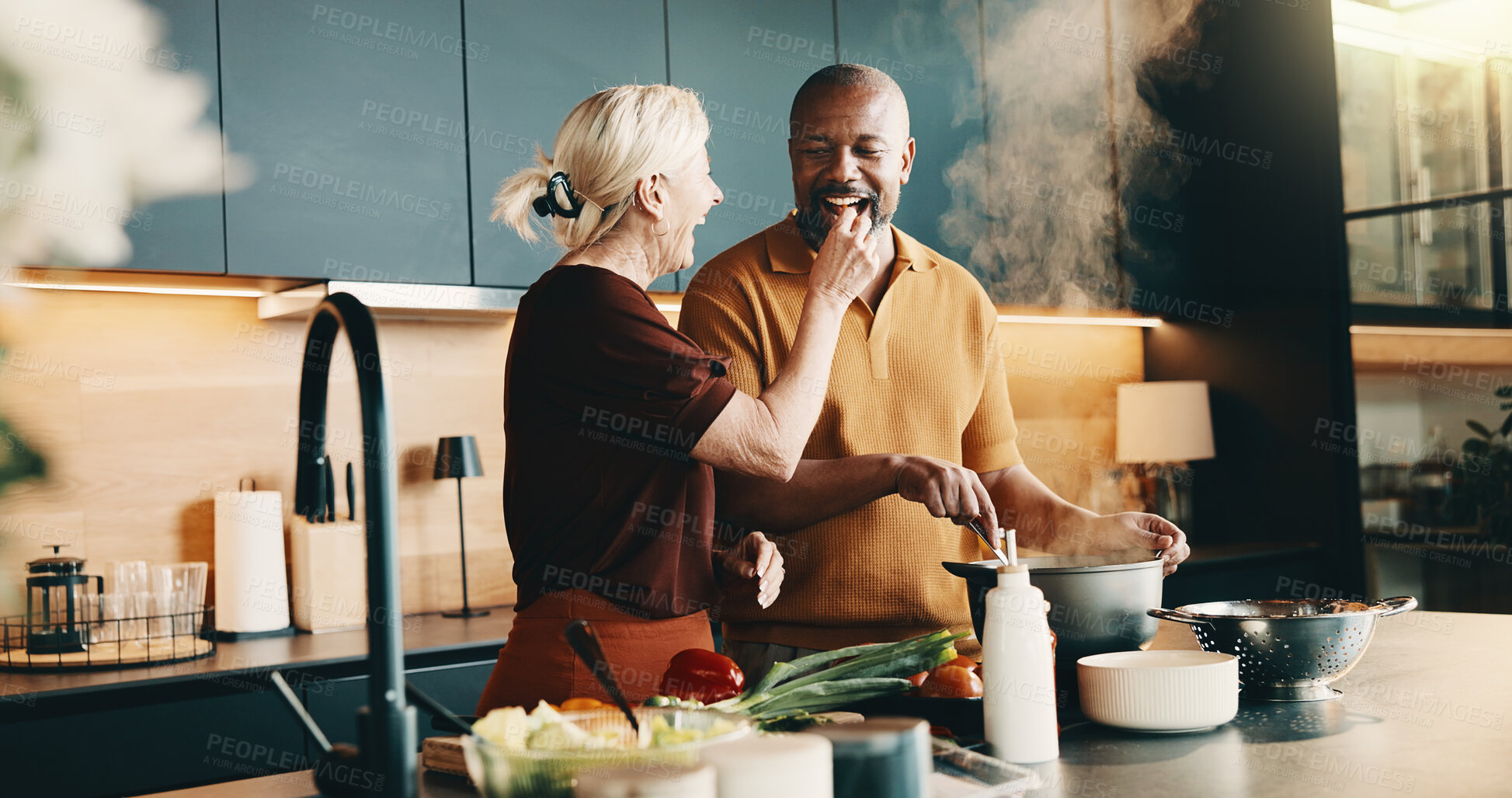 Buy stock photo Cooking, laughing and taste with interracial couple in kitchen of home together for meal preparation. Bonding, feeding and having fun with mature people in apartment for culinary hobby or eating food