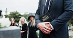 Person, hands and pastor with holy bible for funeral, memorial service or worship of god. Family, people or priest with book, religion or faith at graveyard or cemetery for death or burial ceremony