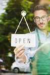 Window, entrepreneur or man with open sign for restaurant, hospitality industry or ready for service. Glass, poster or business owner with welcome message for customer, smile and advertising for cafe