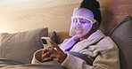 Blue light, skincare and woman with phone in bedroom for beauty, wellness or antibacterial facial. Health, relax and person in bed with LED phototherapy tech for dermatology or mask treatment in home