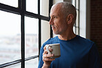 Mature man looking out window drinking coffee at home enjoying relaxed morning planning retirement