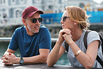 Travel couple on vacation chatting having conversation sitting by table in harbour watefront