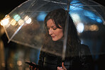 Woman using smartphone texting on mobile phone holding umbrella in rainy city at night