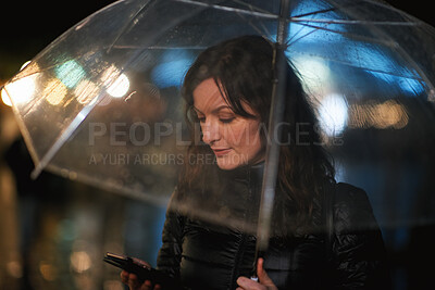 Buy stock photo Online, phone and woman with umbrella in city, communication and checking ride confirmation at night. Dark, outdoor and person with weather protection, bokeh and tracking taxi distance on mobile