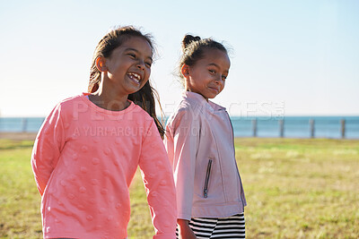 Buy stock photo Happy, girls and siblings playing on grass field by beach for fun childhood, holiday or weekend. People, children or sisters with smile in nature for outdoor bonding, youth or development together