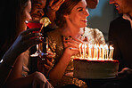 Happy woman dressed in gold smiling at friends holding birthday cake 