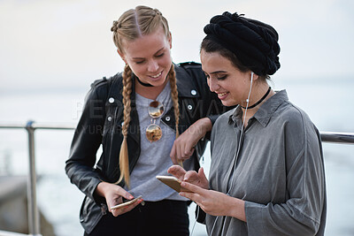 Buy stock photo Phone, friends and women outdoor for music, social media and sharing playlist by promenade. Smile, mobile and girls hangout with audio app, earphones and show podcast info on internet by ocean